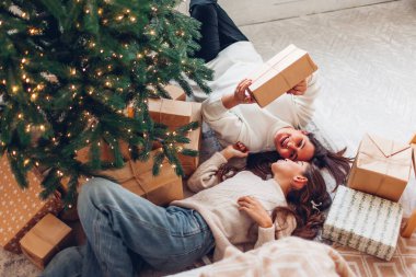 Evde hediye kutularıyla süslenmiş Noel ağacının altında yatan anne-kız manzarası. Çocukla tatil aile zamanı.