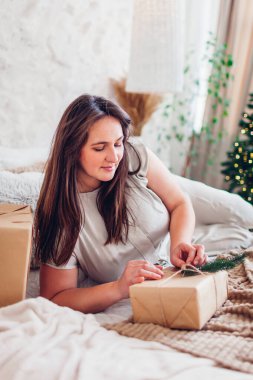 Evde, Noel ağacının yanında uzanmış hediyeleri açan genç bir kadının portresi. Keyifli bir iç mekan