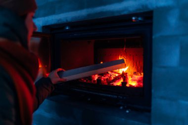 Yeni yapılmış evdeki şömineye odun ekleyen bir kadın. Akşamları ateşi kapat. Konforlu ev oluşturuluyor