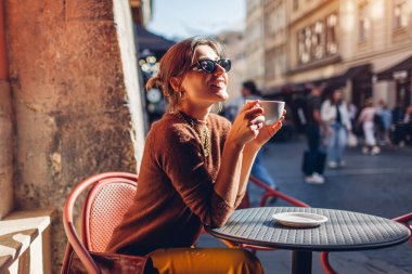 Kafede oturup kahve içen mutlu, şık bir kadın. Lviv şehrinin mimarisinden hoşlanan bir kadın sokakta terasta dinleniyor..