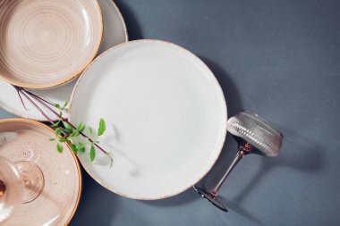 Gri arka planda seramik mutfak malzemelerinin üst görüntüsü. Beyaz, bej benekli yemek takımı ve kokteyl bardaklı çorba tabakları. Boşluk