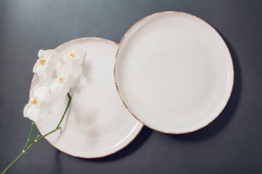 Gri arkaplanda jöleli seramik bulaşık takımının üst görüntüsü. Çiçekli orkidelerle süslenmiş beyaz benekli yemek tabakları.