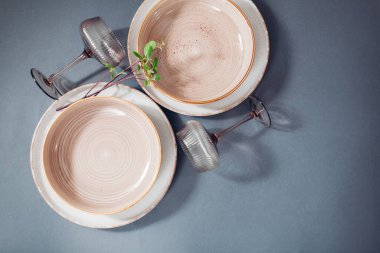 Gri arkaplanda seramik yemek takımının üst görüntüsü. Beyaz, benekli yemek takımı ve bitki dallarıyla süslenmiş kokteyl bardakları. Boşluk