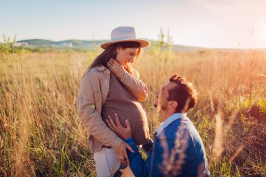 Genç hamile bir çift dışarıda yürüyor. Müstakbel baba eşinin karnına dokunuyor. Evli bir adam ve kadın bebek bekliyor.