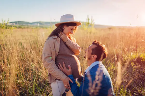 Genç hamile bir çift dışarıda yürüyor. Müstakbel baba eşinin karnına dokunuyor. Evli bir adam ve kadın bebek bekliyor.