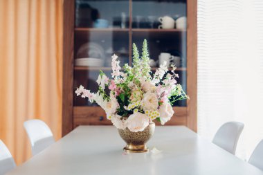 İç dekorasyon. Pirinç vazoda yapılan yaz çiçeği düzenlemesi mutfak gereçleri ile birlikte yemek masasının üstüne koyuldu. Güllü buket, eldivenli.