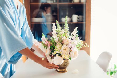 Kadın bir vazo dolusu gül çiçeğiyle birlikte mutfaktaki dolaplara pirinç vazo koyuyor. Ev ve iç dekorasyon. Yaz çiçekleri aranjmanı.