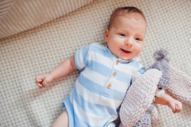 Yeni doğmuş mutlu bebek kanepeye uzanmış, örgü bir oyuncak ve vücut giysisi giyiyor. El yapımı tavşanla oynayan sevimli bir çocuk. Üst görünüm