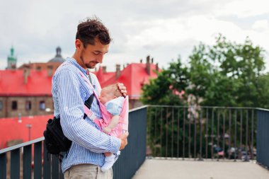 Küçük kız taşıyıcıda uyurken genç baba kızıyla birlikte dışarıda yürüyor. Bebek giyiyorum. Çocuk ebeveyn pozisyonunda. Boşluk