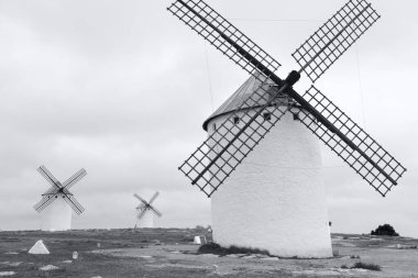 Beyaz rüzgar değirmenleri kırsal alanda bulutlu gökyüzünün altında, siyah ve beyaz fotoğraf