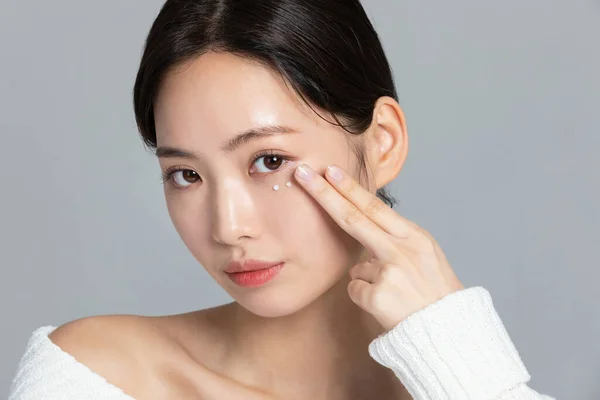 美しい若い韓国人女性のポートレートスタジオ写真で冬の肌の美しさと化粧品のコンセプト_使用アイクリーム — ストック写真