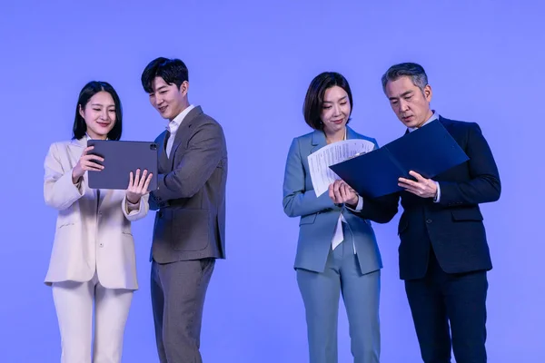 Asian Korean senior, middle aged and young male and female colleagues models in business attire, neon purple studio background, looking at the tablet and the documents concept