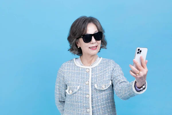 stock image active young senior Korean Asian woman with sunglasses using smartphone