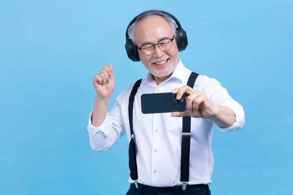 在录音室的背景下 活跃的年轻老年韩国男性 一边用耳机一边用智能手机听音乐 — 图库照片