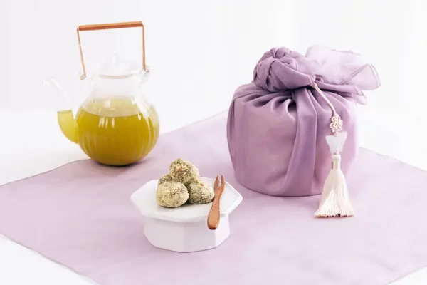 There is a kettle and rice cake around the gift wrapped in cloth