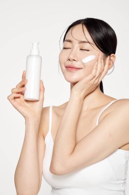 Asian Woman Poses to Apply Cosmetics to Her Face clipart