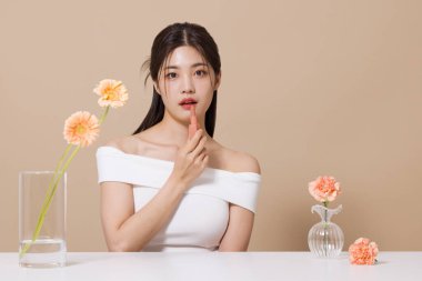 a woman in her 20s holding cosmetics in front of a table decorated with flowers clipart