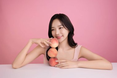 A woman in her 20s posing with a peach on the table clipart