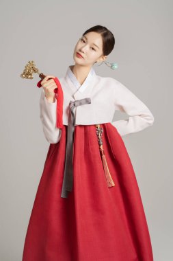 A woman in her 20s wearing a hanbok, wearing a colorful hairpin, and posing while holding a shaman bell. clipart