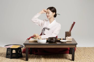 A young shaman sitting in a hanbok in front of a table with shamanic tools spread out and thinking. clipart