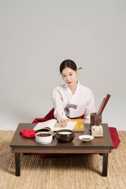 A shaman sitting with an open book and wearing a hanbok and giving advice. clipart