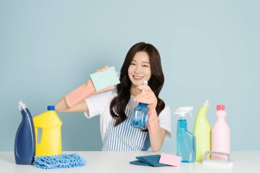 A woman in her 29s sitting in front of a table, wearing rubber gloves and holding a cleaning tool clipart