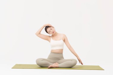 Portrait of a young woman wearing sportswear sitting on a yoga mat and stretching clipart