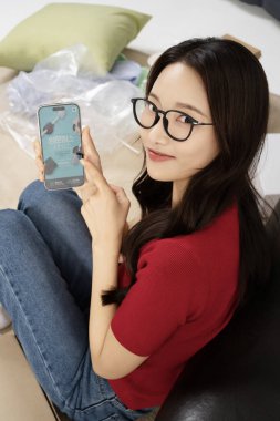 A young man in his 20s using his cell phone in a messy room clipart