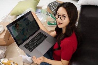 A young man in his 20s looking at a laptop in a messy room clipart