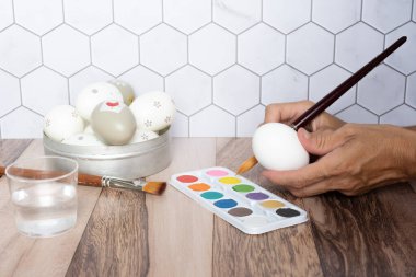 Hands decorating eggs for Easter with a paintbrush and colors.