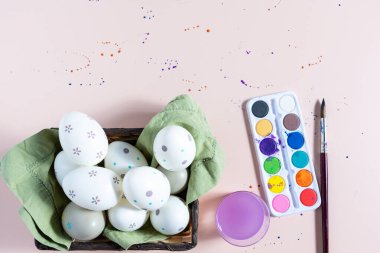 Easter eggs decorated in a basket and painting elements, on a plain background with spots.