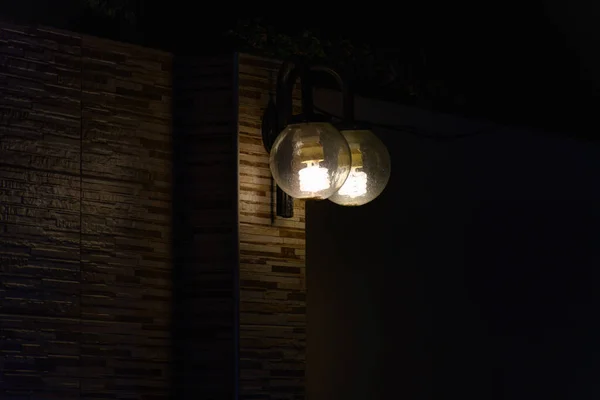 Outdoor lighting fixtures turned on in the dark exterior of a home.