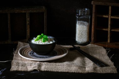 Fesleğen yapraklı beyaz pirinç, yemek çubukları ve altta pişmemiş pirinç kavanozu..