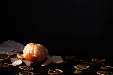 Kurutulmuş turunçgil dilimleriyle çevrili yarı soyulmuş mandalina portakallarına odaklan. Işıklar ve gölgeler koyu yiyecek tarzı.