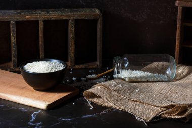 Tepetaklak kavanoz, tahta kaşık ve çiğ beyaz yamani pilavlı siyah kase..