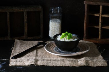 Fesleğen yapraklı beyaz pirinç, yemek çubukları ve altta pişmemiş pirinç kavanozu..