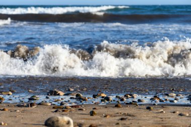 Arka planda dalgakıran olan kumsalın kum ve taşlarına odaklan..
