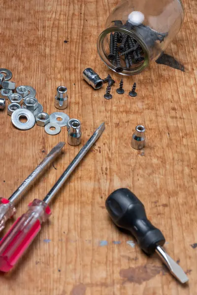 Screwdrivers, screws, socket wrenches and washers on a rustic workbench.