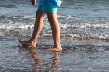 Deniz kıyısında yürüyen bir gencin ayakları.
