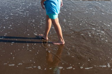 Deniz kıyısında yürüyen bir gencin ayakları.