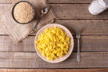 Sarı pirinçli ve safranlı bir tabağın üst görüntüsü, bir kasede pişmemiş pirinç, tuz kavanozu ve çatal bıçak takımı..