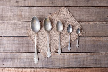 Çuval bezi ve kırsal ahşap üzerinde farklı boyutlarda antika alpaka kaşıkları serisi.