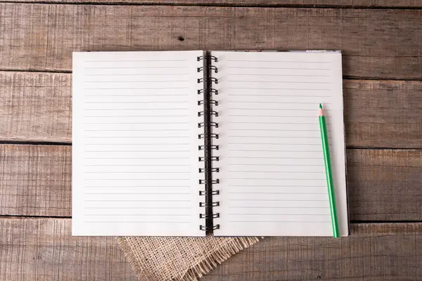 Astarlı sayfaları olan sarmal defter ve kırsal ahşap üzerine yeşil bir kalem..