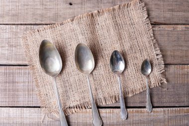 Çuval bezi ve kırsal ahşap üzerinde farklı boyutlarda antika alpaka kaşıkları serisi.