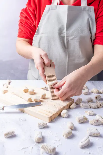 Mutfak önlüğü giymiş biri patates gnocchi şekillendiriyor..