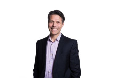 Beyaz arka planda kameraya gülümseyen orta yaşlı bir adam, resmi kıyafetler giyiyor..