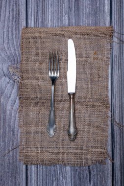 Çuval masa örtüsündeki alpaka metal bıçak ve çatalın üst görüntüsü.
