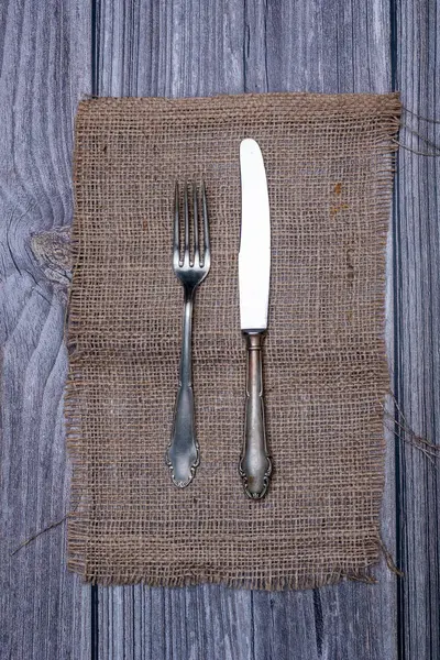 Çuval masa örtüsündeki alpaka metal bıçak ve çatalın üst görüntüsü.