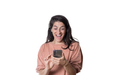 Beyaz arka plandaki kadın, akıllı telefonuna şaşkın neşeli bakıyor..