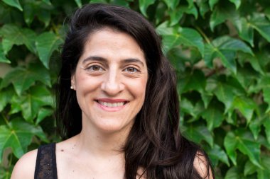 Arka planda bitki örtüsüyle gülen bir kadının yakın çekimi..